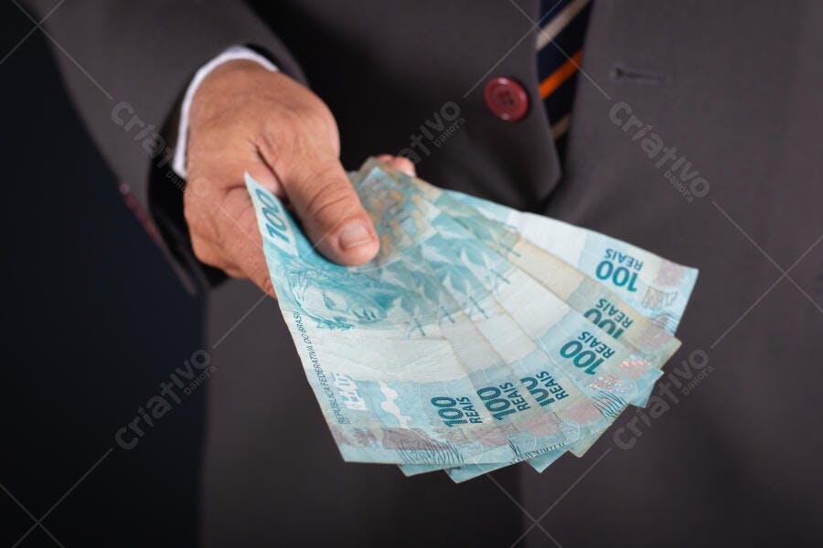 Homem de terno cinza segurando notas de 100 Reais em transação financeira