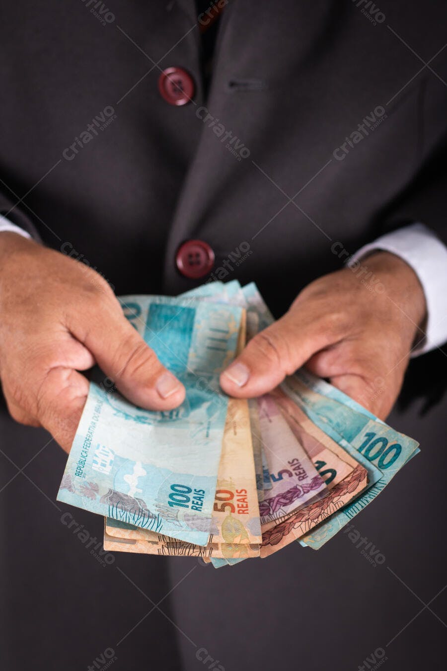Mãos de empresário segurando notas de reais dinheiro brasileiro azul e dourado