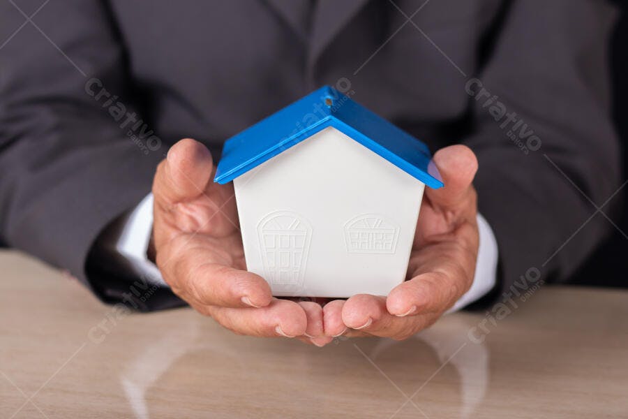 Homem de terno segurando casa miniatura com telhado azul
