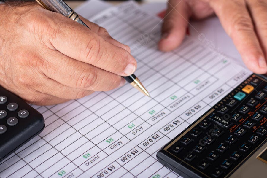 Mão masculina escrevendo em planilha financeira com calculadora no escritório