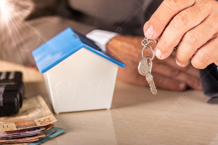 Chaves de casa azul e branca com notas de reais em uma mesa de negociação