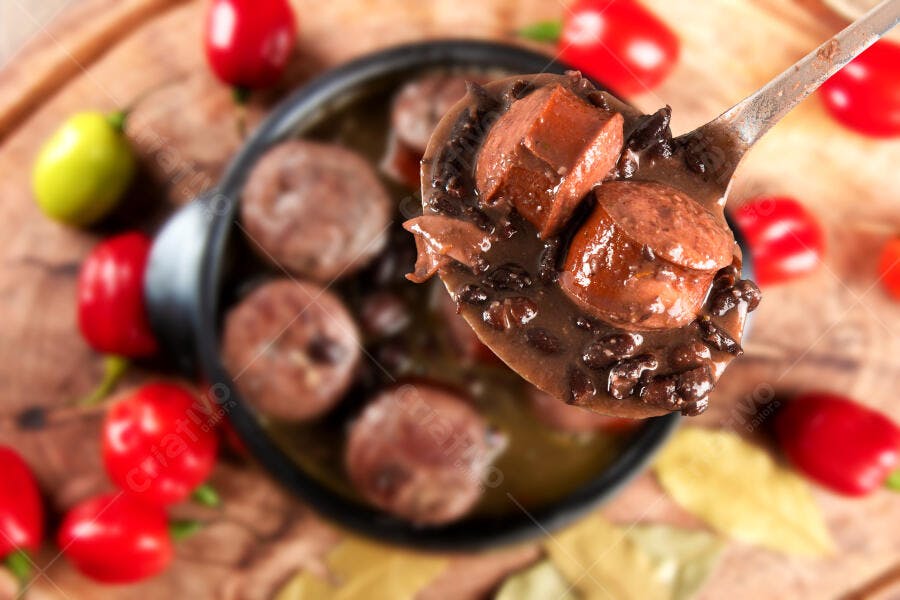 Feijoada brasileira sendo servida com pimenta em tábua de madeira rústica