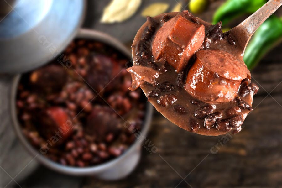 Feijoada brasileira sendo servida em colher grande com linguiça e carne suína