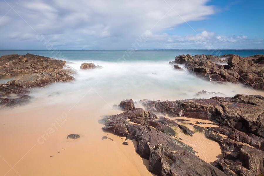 Paisagem costeira rochosa com mar turvo e areia dourada