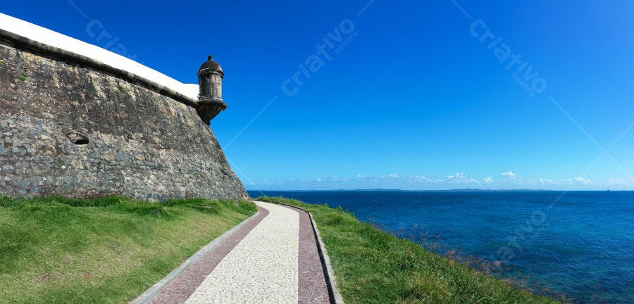 Muralha de forte histórico com torre de vigia caminho e oceano azul claro