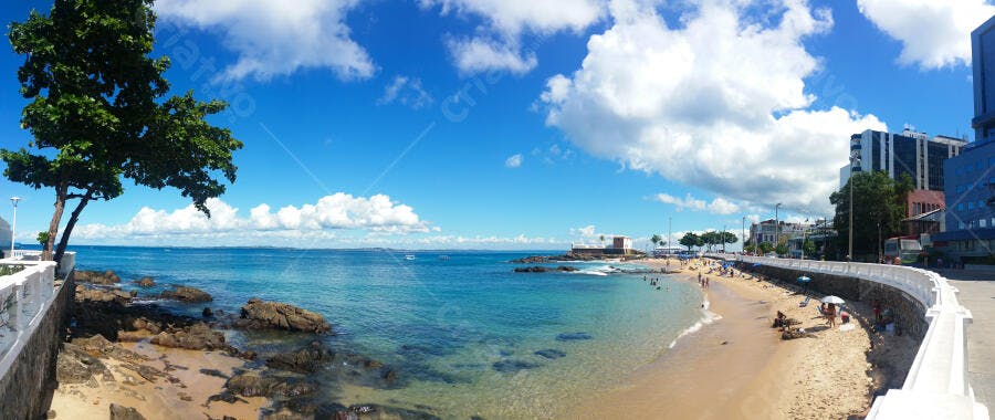 Praia urbana ensolarada com banhistas nadando e prédios na costa