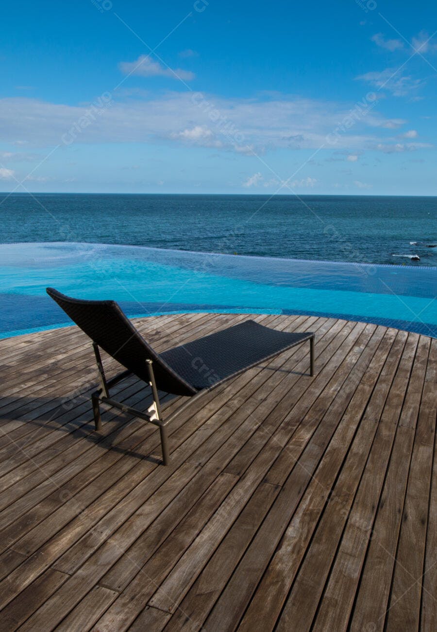 Chaise espreguiçadeira em deck de madeira com piscina de borda infinita e mar azul