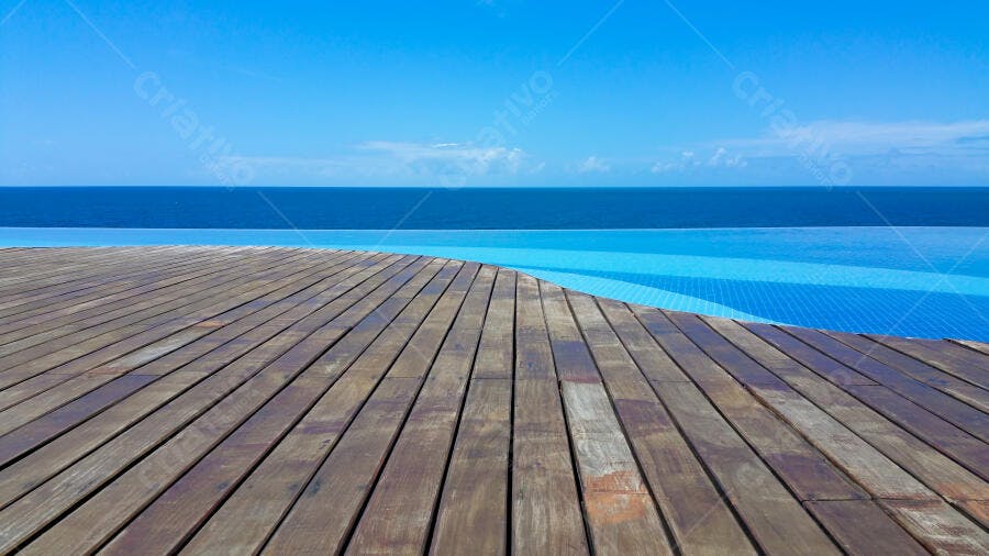 Piscina de borda infinita com deck de madeira e oceano azul claro