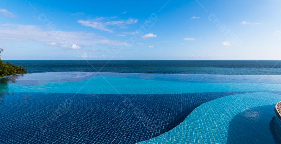 Piscina infinita com vista para oceano azul tropical sob céu claro e sol