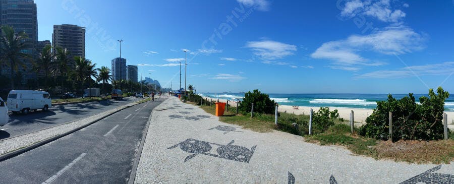 Calçadão de praia urbana com mosaico, mar azul, prédios e palmeiras em dia ensolarado