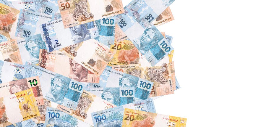 Notas de Real brasileiras espalhadas sobre fundo branco azul e marrom claro