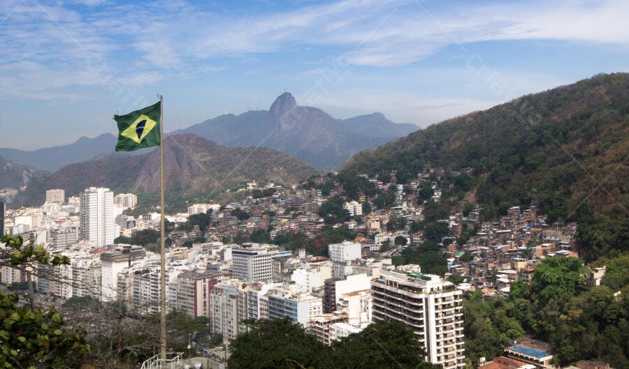 Bandeira do Brasil em vista panorâmica do Rio de Janeiro com prédios e favela sob céu azul