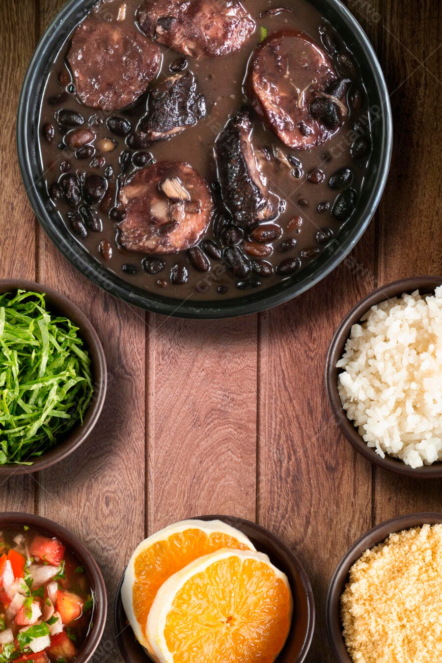 Feijoada brasileira completa com arroz, couve, farofa e laranja em mesa de madeira rústica
