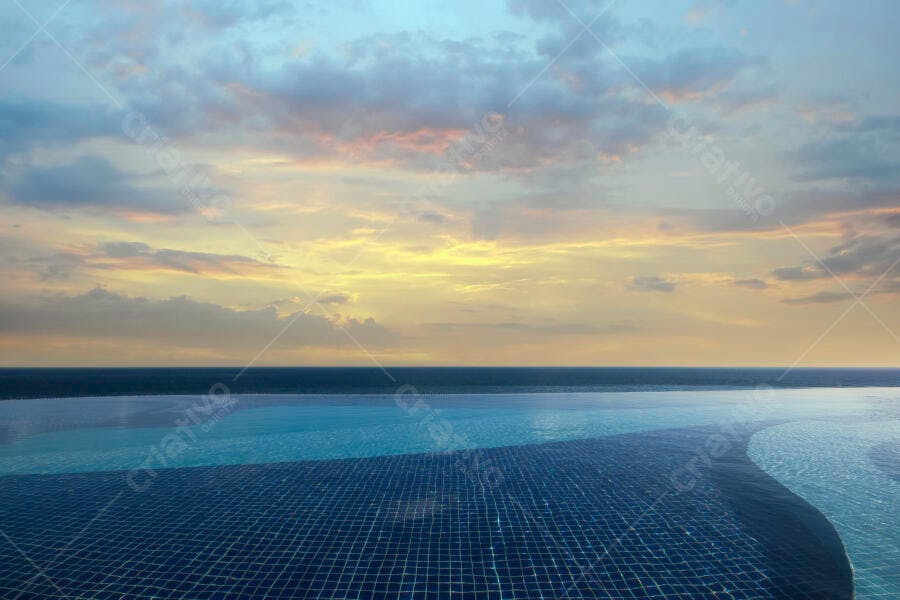 Piscina de borda infinita azul com vista para o mar ao pôr do sol colorido e sereno