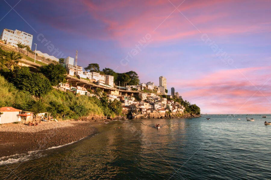 Pôr do sol rosa sobre cidade costeira com casas na encosta e barcos no mar