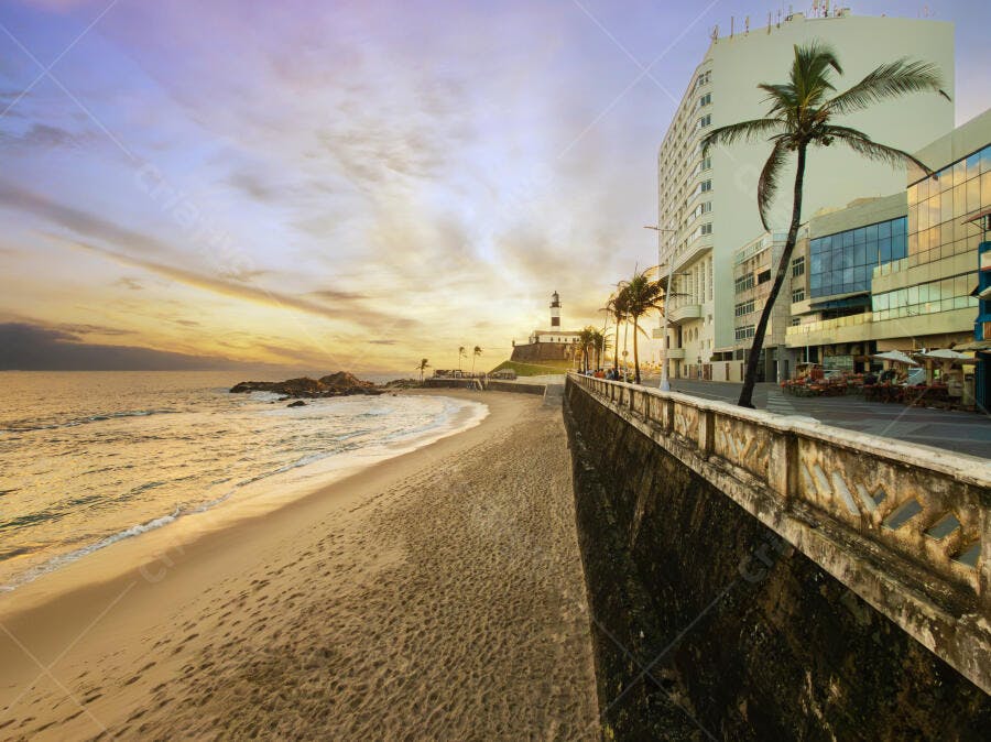 Farol da Barra na praia urbana ao pôr do sol com céu laranja e roxo