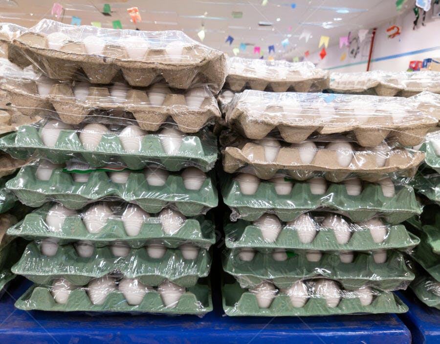 Cartons de ovos brancos empilhados em supermercado com embalagens verdes e marrons