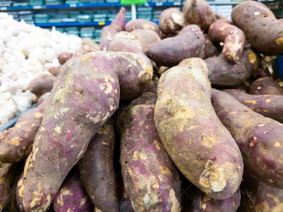 Batatas doces roxas frescas empilhadas em mercado de hortifruti