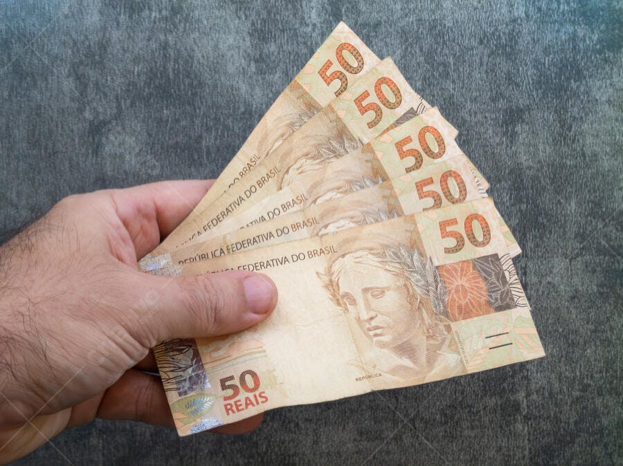 Mão segurando várias notas de 50 Reais brasileiros dinheiro em fundo escuro