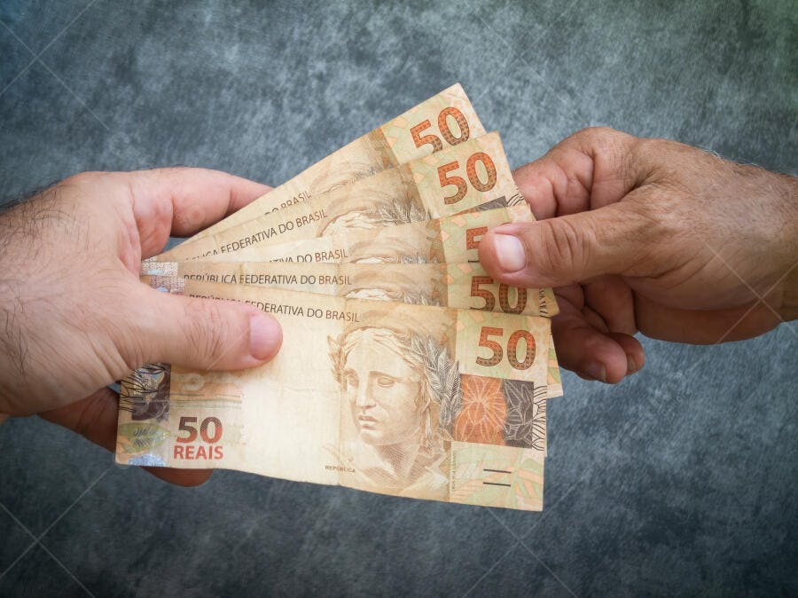 Mãos trocando notas de cinquenta Reais brasileiros sobre fundo cinza
