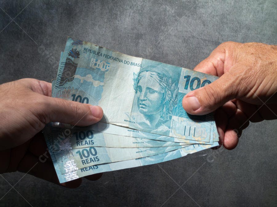 Notas de 100 reais azuis sendo trocadas entre mãos em um fundo escuro