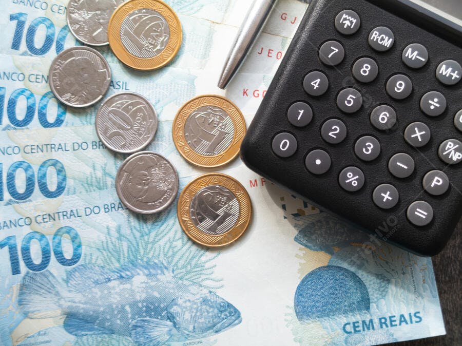 Dinheiro brasileiro notas de cem reais e moedas douradas prata com calculadora preta