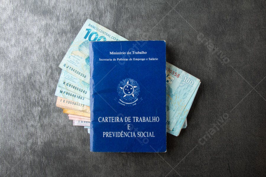 Carteira de Trabalho azul com dinheiro brasileiro Real sobre fundo escuro