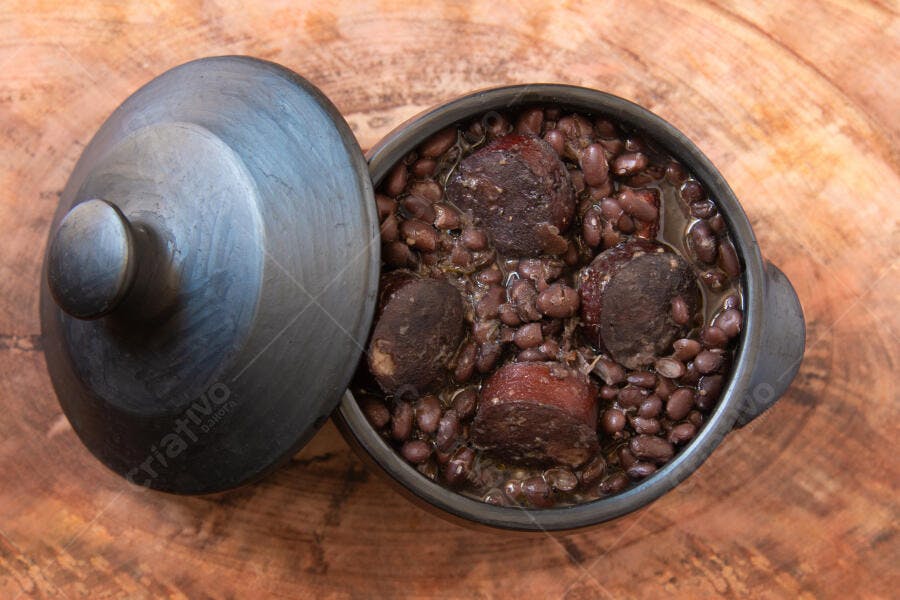 Panela de barro com feijoada caseira sobre mesa de madeira rústica