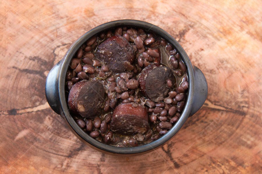 Panela de barro com feijão preto e linguiça sobre tábua rústica