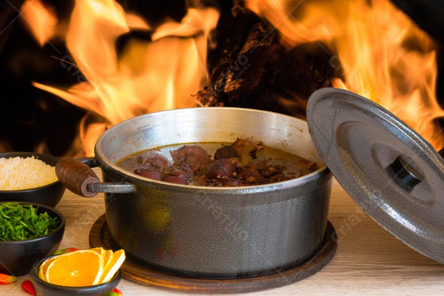 Caldeirão de feijoada tradicional com acompanhamentos e fogo aceso no inverno