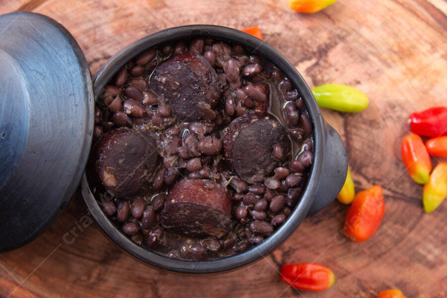 Feijoada em panela de barro com linguiça e pimentas coloridas sobre mesa de madeira