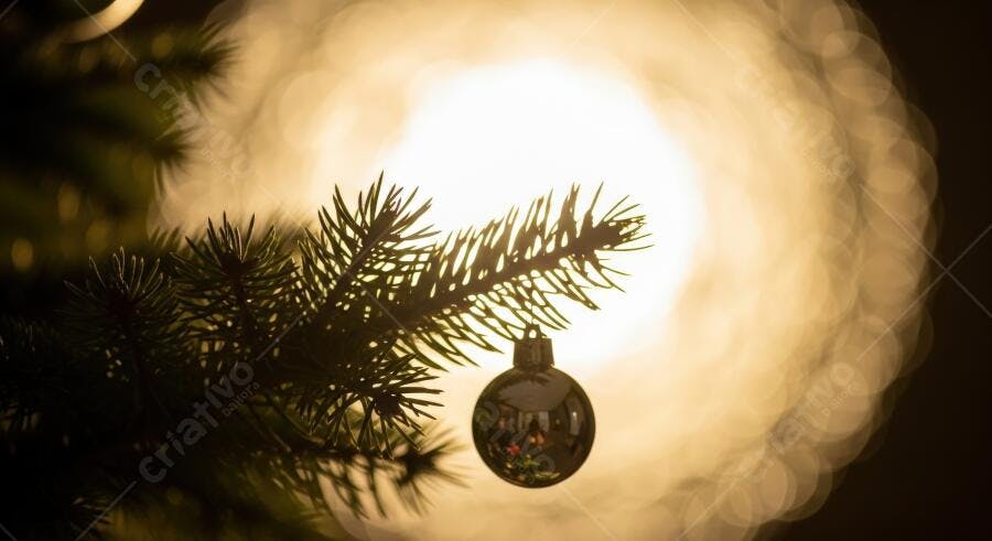 Galho de árvore de Natal com bola prateada e luz dourada desfocada