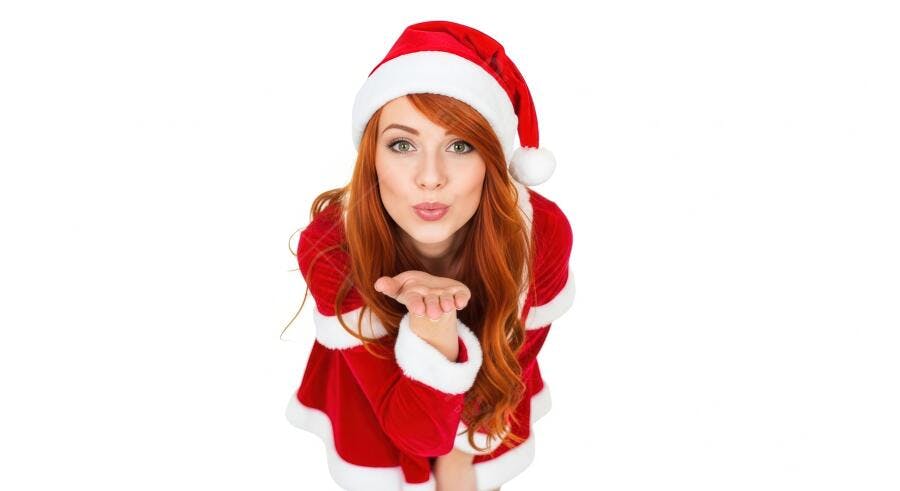 Mulher ruiva vestida de Mamãe Noel mandando beijo no Natal