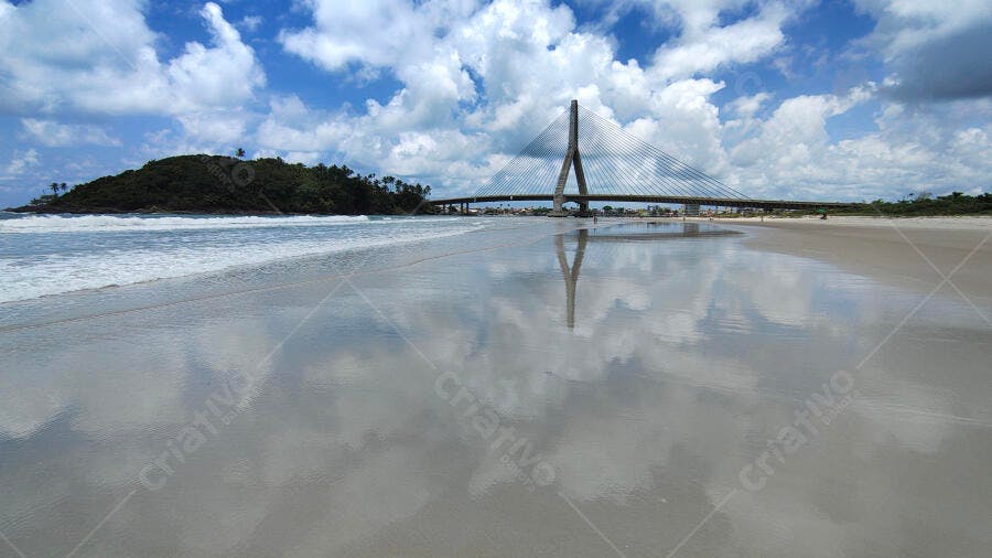 Ponte estaiada moderna na praia com céu azul e reflexo na areia molhada