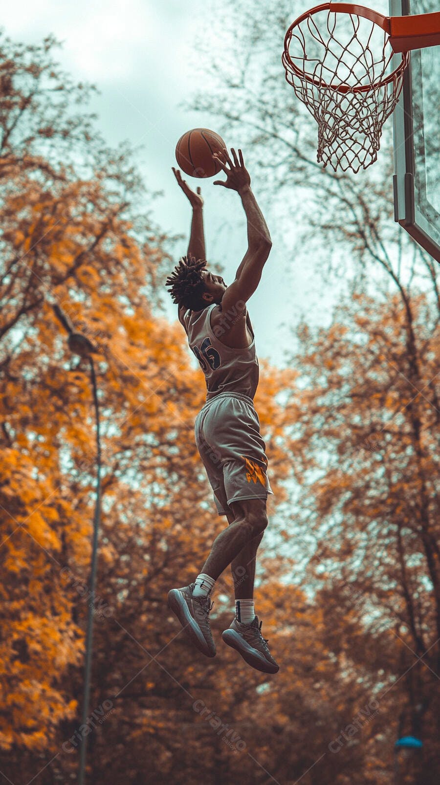 Homem negro jogador de basquete pulando para cesta em quadra com árvores outonais
