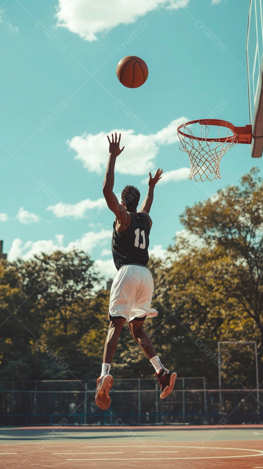 Homem afro-americano pulando para arremessar bola de basquete em quadra ao ar livre