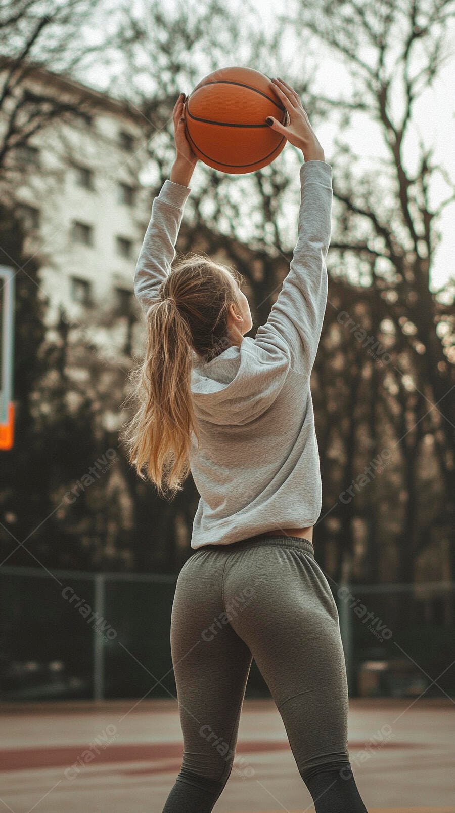Mulher loira com moletom cinza arremessando bola de basquete em quadra ao ar livre