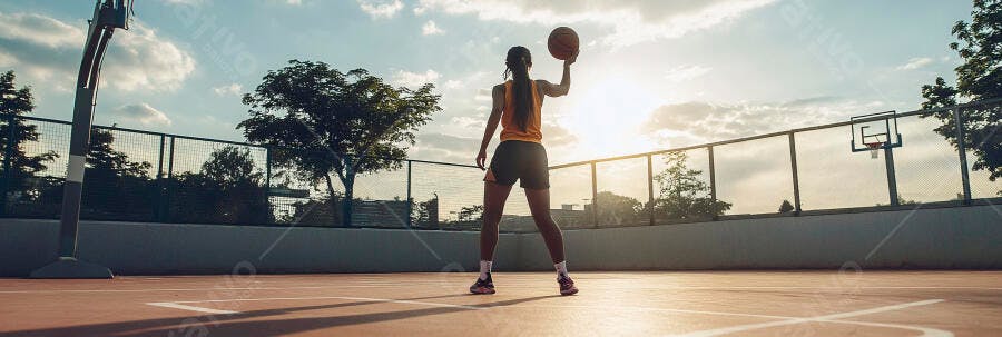 Jovem mulher atlética jogando basquete em quadra ao pôr do sol dourado