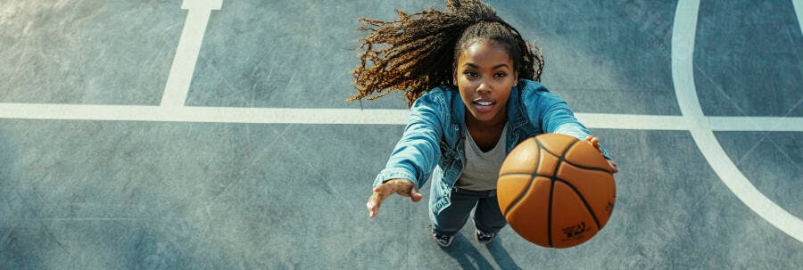 Jovem mulher negra jogando basquete na quadra urbana com jaqueta jeans azul