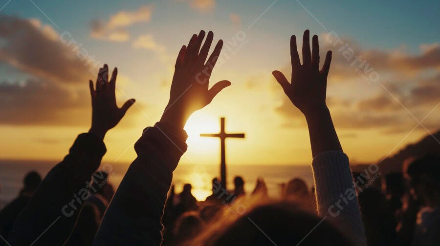 Pessoas com mãos erguidas adorando uma cruz ao pôr do sol dourado
