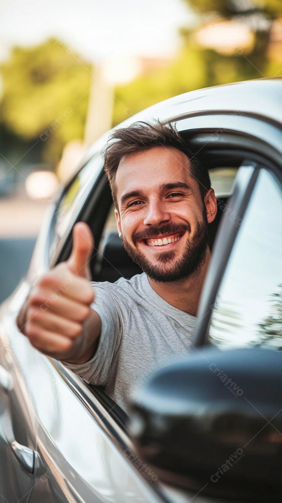 Homem sorridente de camiseta cinza no carro com polegar para cima