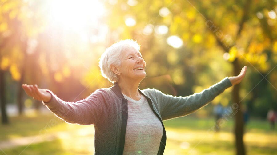 Mulher idosa sorrindo com braços abertos na luz dourada do outono