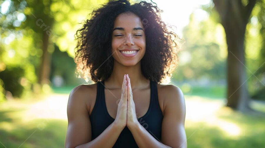 Mulher negra de cabelo cacheado sorrindo em pose de meditação e yoga no parque