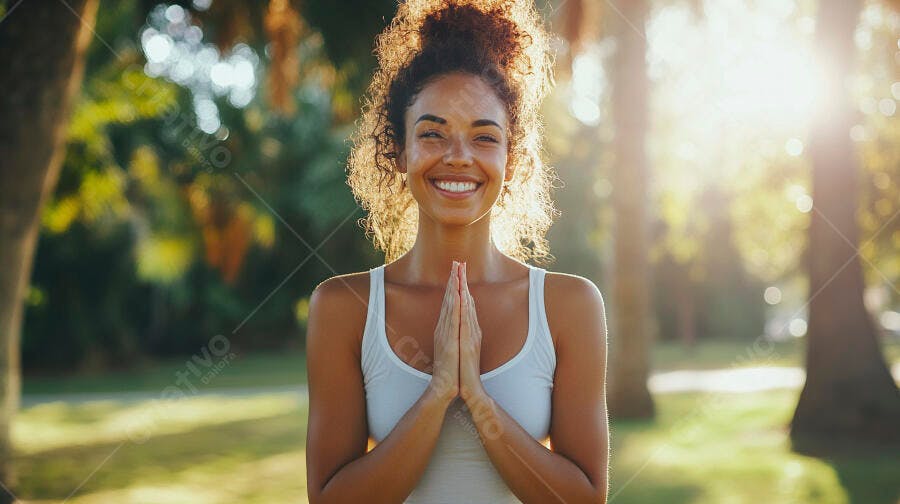 Mulher negra sorrindo com mãos em oração em parque ensolarado ao entardecer
