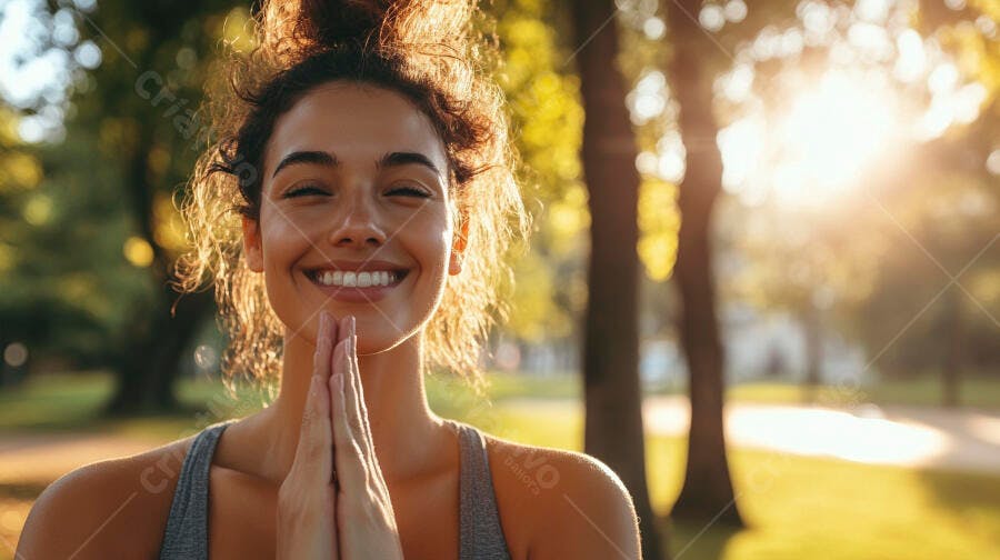 Mulher jovem morena sorrindo com mãos em prece no parque ao sol dourado