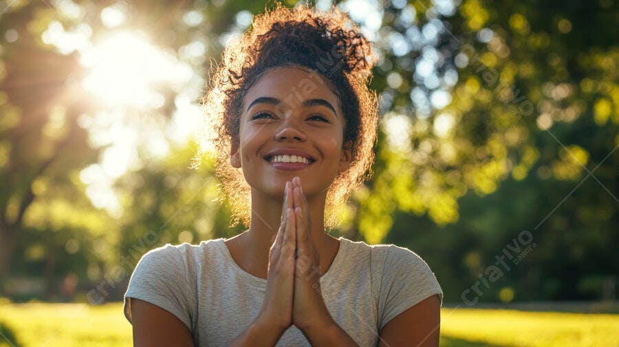 Mulher feliz com cabelo encaracolado orando em parque ensolarado