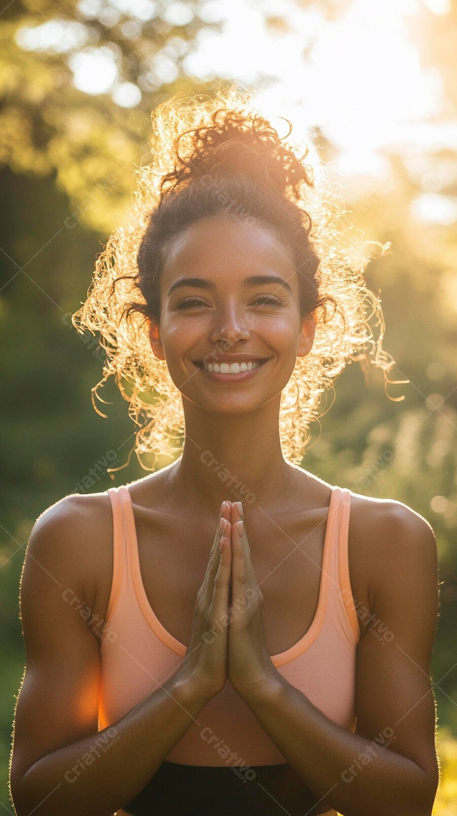 Mulher sorridente com cabelo cacheado em pose namaste ao pôr do sol