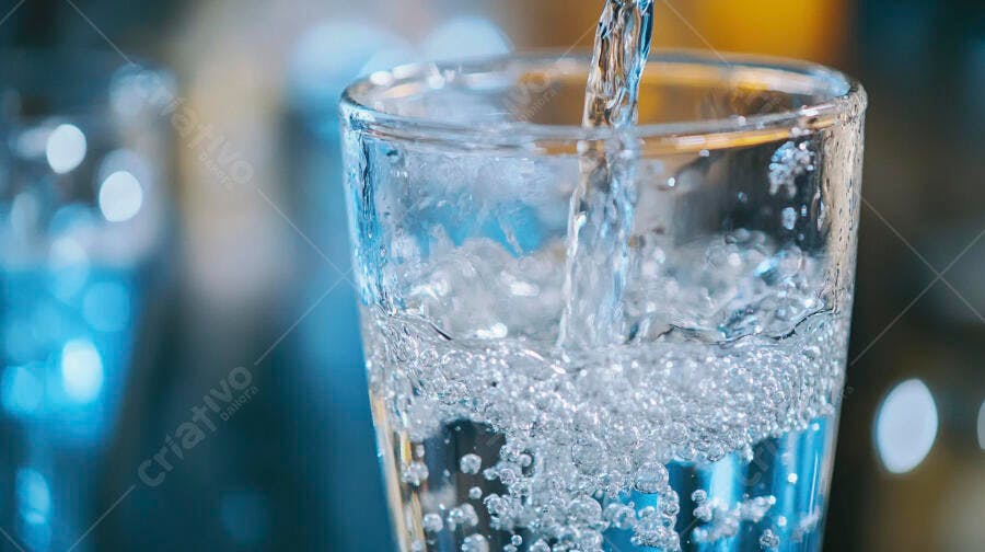 Água sendo despejada em copo de vidro transparente criando bolhas com fundo azul desfocado