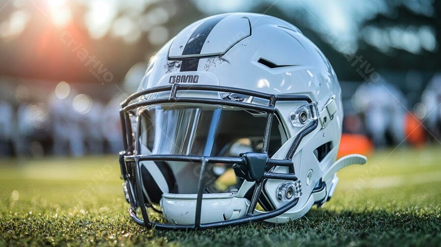 Capacete futebol americano branco com riscos no gramado ao pôr do sol