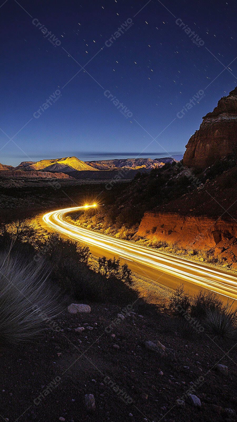 Estrada sinuosa com rastros de luzes de carro no deserto à noite sob céu estrelado